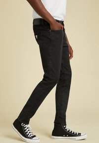 Jeans in denim nero con una vestibilità aderente. Presentano cinque tasche, passanti per la cintura e un'etichetta sul retro. Abbinati a sneakers nere alte.