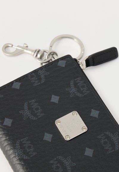 Μαύρο δερμάτινο θήκη για κλειδιά με υφή, με ασημένια πλακέτα λογότυπου MCM, εγχάραξη με λεπτομέρειες της μάρκας και μεταλλικό κρίκο κλειδιών με αναδιπλούμενο κούμπωμα.