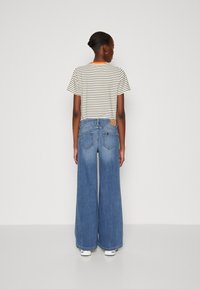 Camiseta de rayas de manga corta con cuello naranja, combinada con unos pantalones vaqueros de pierna ancha azul con bolsillos traseros y una etiqueta de marca en tono marrón.