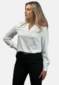 Biała bluzka z długim rękawem z dekoltem w kształcie łezki i gładką fakturą, zestawiona z czarnymi spodniami o wysokim stanie.