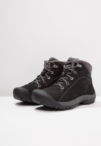 Botas de senderismo de ante negro con cordones grises y un collar acolchado. Suela de goma gruesa para mayor tracción. Presenta ojales de metal y un logo lateral.
