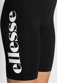 Svarta träningsshorts med en åtsittande design, utrustade med en vit "ellesse"-logotyp som är tryckt vertikalt. Tillverkade av ett stretchigt tyg med en smooth yta.