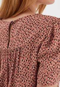 Tessuto rosa con motivo a pois neri e crema, caratterizzato da un dettaglio a chiave sulla schiena e una linea gather sulle spalle.