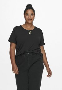 Black t-shirt with rolled sleeves, made of soft cotton, paired with black pants. Simple design, smooth texture, subtle round neckline.