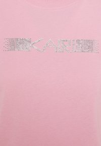 Camiseta rosa de textura suave con la palabra "KARL" en brillantes rhinestones plateados en el pecho. Manga corta y escote redondo.