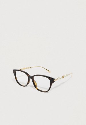 Želve oči z квадратnimi okvirji, zlate temples okrašene s perlicami in malimi zlatimi okraski na belem ozadju.