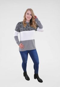 Grijze en witte trui met een luipaardprint ontwerp, gecombineerd met blauwe jeans en zwarte enkelboots. Soepele textuur, casual pasvorm.