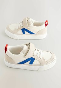 Sneakers na rzepy z beżowo-białą cholewką z płótna, niebieskim paskiem akcentującym i czerwoną pętelką na pięcie. Biała gumowa podeszwa.