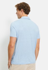 Polo blu chiaro a maniche corte con finitura testurizzata, dotato di un colletto classico e spacchi laterali sul fondo per un maggiore comfort.
