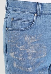 Světle modré džíny z denimu s vybledlým vzorem, designem s pěti kapsami a stříbrným knoflíkem na zapínání v pase.