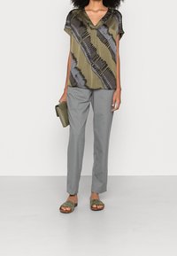 Olivegrön silkesblus med svart randmönster, i kombination med ljusgrå skräddarsydda byxor och olivegröna sandaler. Inga ytterligare accessoarer.