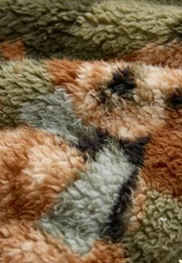 Close-up of a soft, multicolored textured fabric with orange, green, beige, brown, and black patterns.