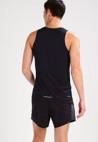 Débardeur de sport noir sans manches en tissu évacuant l'humidité, avec un accent réfléchissant près de l'ourlet, accompagné d'un short noir.
