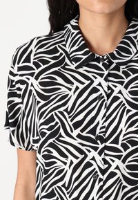 Κοντομάνικη μπλούζα από ελαφρύ ύφασμα, με έντονο αφηρημένο μοτίβο σε μαύρο και λευκό χρώμα, κολαριστό λαιμό και κλείσιμο με κουμπί.