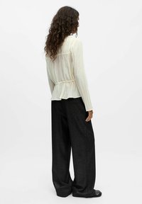 Blouse crème légère et texturée avec taille froncée, associée à un pantalon noir évasé avec un léger brillant. La silhouette est décontractée.
