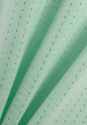 Lichtgroene stof met kleine, gelijkmatig verdeelde perforaties, getoond in zachte plooien die de textuur en ademend materiaal benadrukken.