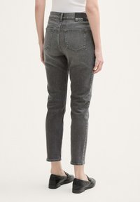 Jeans de mezclilla gris con un ajuste slim, diseño de cinco bolsillos y una etiqueta en la cinturilla. La tela tiene una ligera textura y un acabado suave.