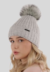 Berretto a maglia grigio con un design a coste, caratterizzato da un morbido pon pon in pelliccia grigia sulla sommità e da una piccola targhetta nera sul lato.