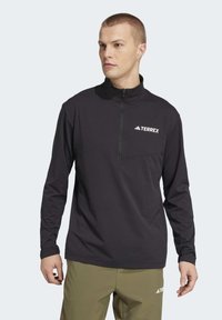 Black long-sleeve half-zip pullover made of soft material, featuring a chest pocket and white TERREX logo on the left side.