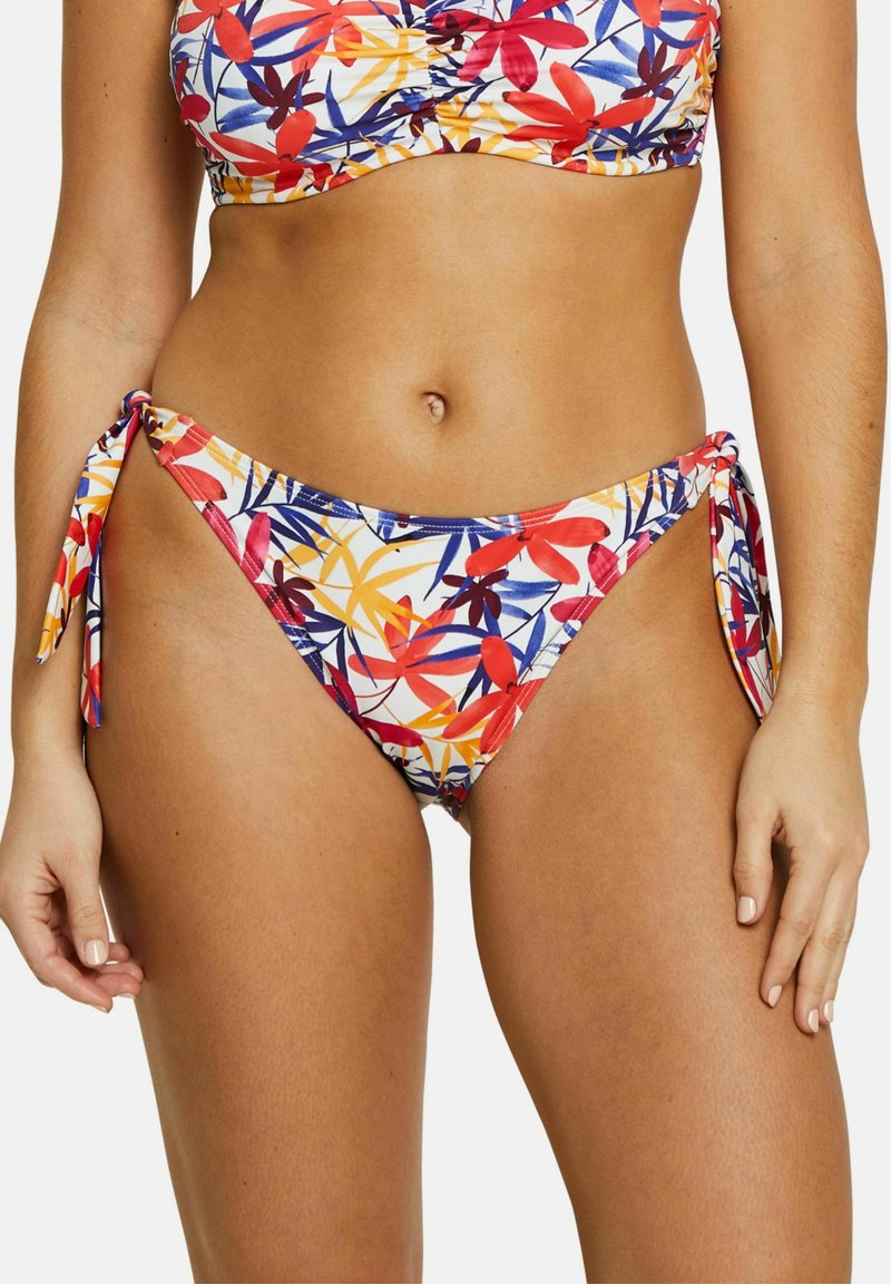 Bas de bikini fleuri avec un motif de feuilles multicolores en rouge, orange et bleu. Le tissu est extensible avec des accents de liens sur les côtés.