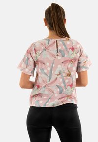 Top floreale a maniche corte di colore rosa, con motivo a pois, dettaglio con apertura a chiave sul retro e tessuto morbido con una sottile lucentezza.