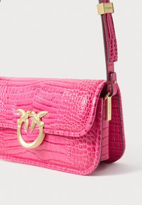 Bolsa de mão em pele com padrão de crocodilo rosa, com um fecho dourado em forma de folha, alça ajustável e um acabamento liso e brilhante.