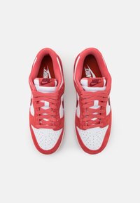 Röda mockaskor och vita läderskor med låg design, perforerat tåparti och kontrasterande snören med en logotyp på tungan.