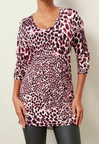 T-shirt à manches longues et décolleté en V, arborant un imprimé léopard rose et noir sur un matériau doux et texturé. Coupe ample avec un ourlet arrondi.