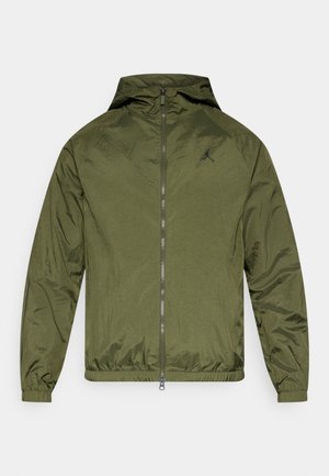 Ελαφρύ μπουφάν με κουκούλα σε ελιά πράσινο χρώμα, με μπροστινό φερμουάρ, ελαστικά μανίκια και ένα μικρό μαύρο λογότυπο στο στήθος. Ομαλή, γυαλιστερή υφή.