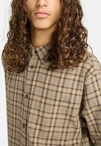 Braun- und beige-karierter Hemd mit Button-Down-Kragen, ausgestattet mit dunklen Knöpfen und einem strukturierten Stoff mit ausgeprägten Rautenmuster.