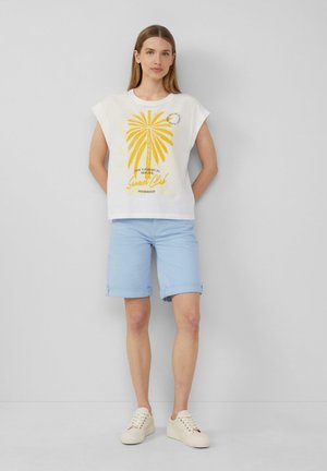 T-shirt blanc à manches courtes avec un graphique de palmier jaune, associé à un short bleu clair. Les chaussures sont des sneakers couleur crème.