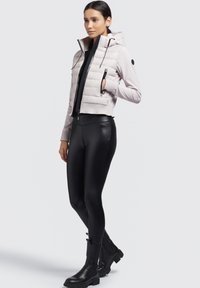 Gepolsterte, cropped Jacke in Hellrosa mit Kapuze, Reißverschlusstaschen und gerippten Bündchen, kombiniert mit hochgeschnittenen schwarzen Leggings und schwarzen Knöchelstiefeln.