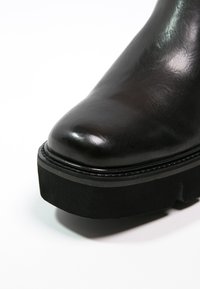 Botte en cuir noir poli avec une semelle plateforme épaisse et un bout arrondi, présentée en gros plan sur un fond blanc.