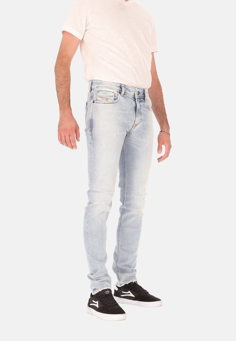 Lichtblauwe spijkerbroek met een slanke pasvorm, voorzien van contrasterende stiksels en een standaard ontwerp met vijf zakken, gecombineerd met een lichtgekleurde T-shirt en zwarte sneakers.