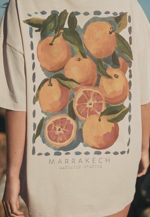 Beiges Hemd mit künstlerischem Design ganzer und geschnittener Mandarinen mit grünen Blättern und dem Text "MARRAKECH MANDARIN ORANGES" darunter.