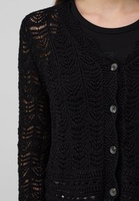 Black knit cardigan with elaborate lace pattern, featuring a v-neckline and four decorative buttons down the front.
