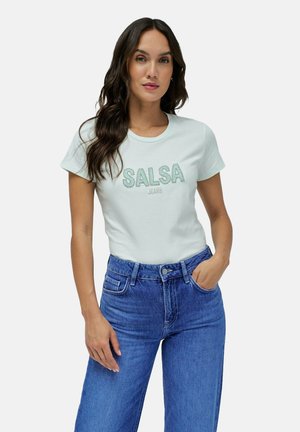 Camiseta de manga corta verde claro con "SALSA" y "JEANS" bordado en verde más oscuro, combinada con jeans de denim azul de cintura alta.