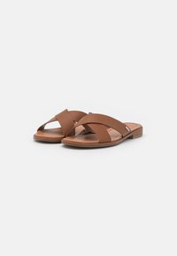 Sandales à glissière en cuir marron avec un design à lanières croisées et une surface texturée. Talon bas avec un bout rond et une semelle intérieure lisse.