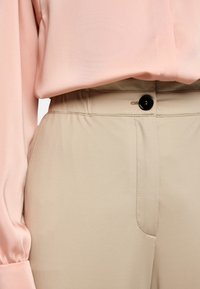 Light pink blouse with long sleeves, paired with beige trousers featuring a button closure and soft, smooth fabric.
