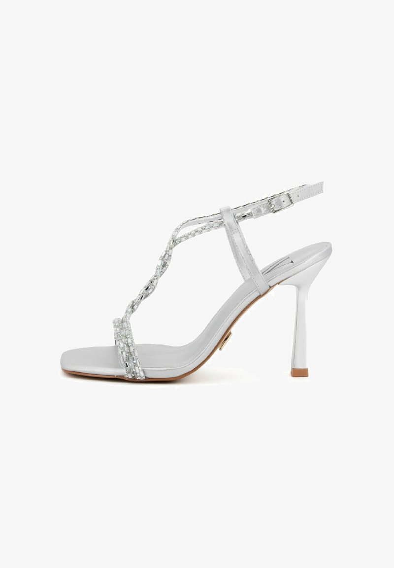 Sandalo argento con tacco alto a stiletto sottile, cinturini con perline e fibbia regolabile alla caviglia. Texture morbida e design minimalista.