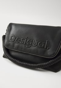 Crna kožna torbica s utisnutim logotipom "Desigual", s teksturiranom površinom, zatvaranjem na zip i spiralnom ručkom.