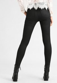 Jeans skinny negros con cintura alta y una textura suave, combinados con botas de tobillo negras. Los bolsillos traseros cuentan con costuras curvas.