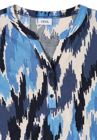 Chemise avec un motif abstrait en zigzag bleu, marine, gris et beige, encolure Henley avec trois boutons marine, et une étiquette de marque "CECIL".
