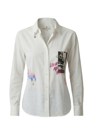 Camisa blanca de botones con texto gráfico, una impresión en foto en blanco y negro, un detalle de imperdible y un pequeño pin de estrella en el cuello.