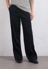 Zwarte, wijde broek met elastische tailleband, gemaakt van een gladde stof, gecombineerd met een gestreepte, loszittende top.