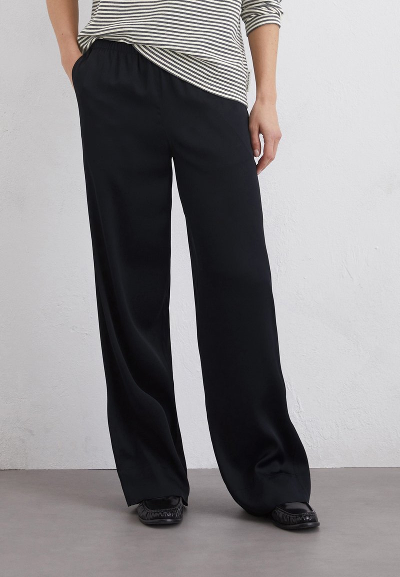 Zwarte, wijde broek met elastische tailleband, gemaakt van een gladde stof, gecombineerd met een gestreepte, loszittende top.