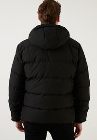 Sort puffjakke med hætte, der har et quiltet design og ribbet struktur, som viser en løs pasform med markante sømme og polstring.