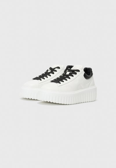 Valged sneakers mustrate mustade aktsentidega, tekstureeritud tallaga ja ümmarguse varbaga. Omab musti lipsusid ja sileda nahkviimistlust. Minimalistlik disain.
