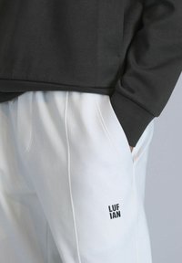 Zwarte sweatshirt met een ronde hals, gecombineerd met witte sweatpants. De broek heeft zijzakken en een zwart logo op het onderbeen.