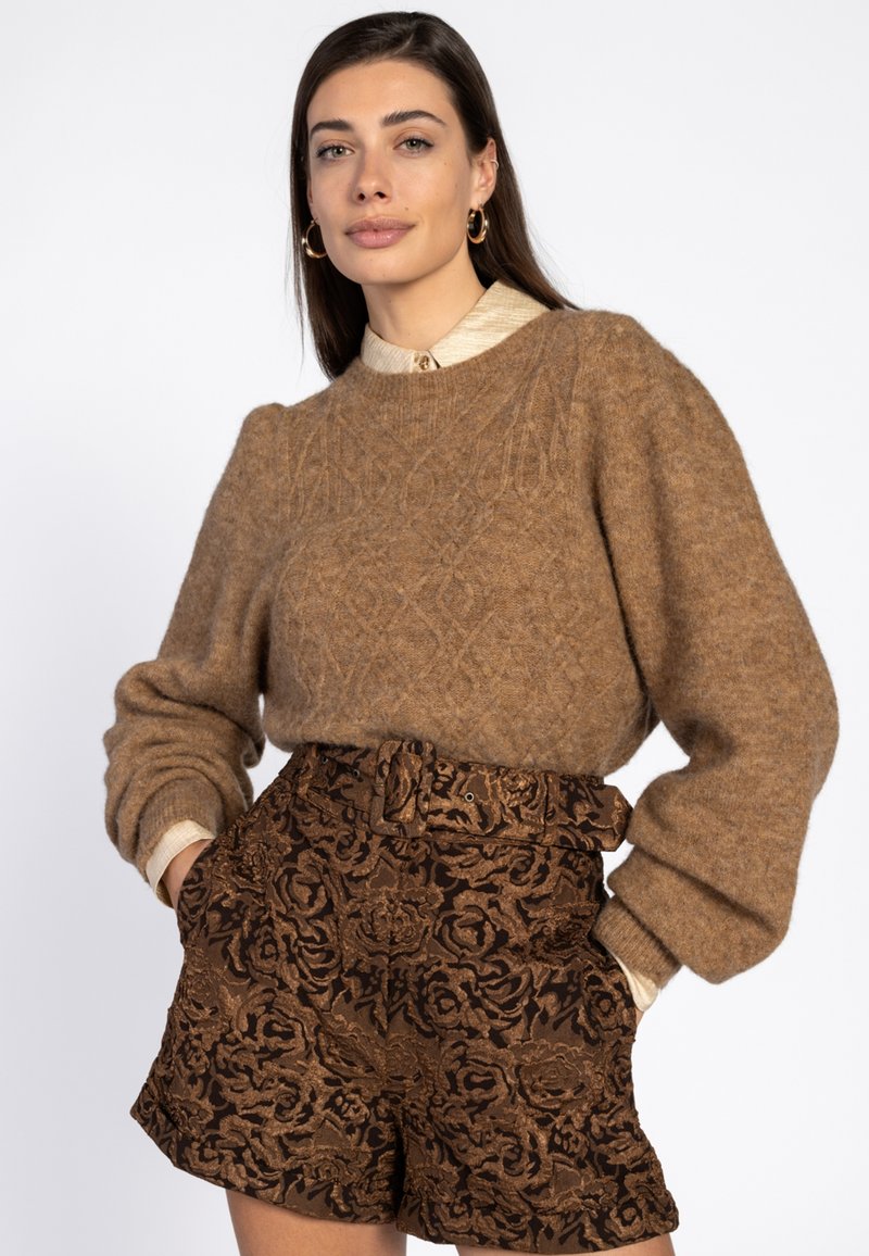 Bruine gebreide trui met een gestructureerd ruitpatroon en pofmouwen, gecombineerd met bruine shorts met bloemenembossing en een licht overhemd met kraag.